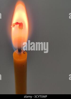 Die Kerze brennt. Eine helle, lang gestreckte Flamme ist deutlich sichtbar und hat eine satte gelb-orange Farbe mit einem weißen Kern. Stockfoto