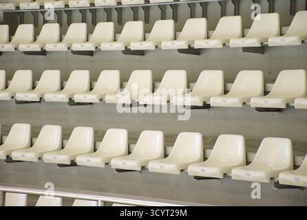 Leere weiße Kunststoffsitze, die in perfekten Reihen in einer modernen Sportarena oder einem Stadion angeordnet sind. Sauberer und minimaler Hintergrund. Sportveranstaltungen, Wettkämpfe Stockfoto