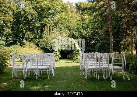 Hochzeitszeremonie im Freien mit weißen Stühlen und Blumenbogen. Stockfoto