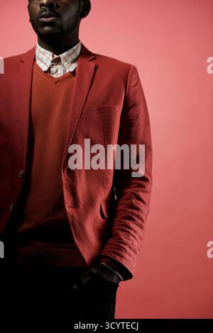 Porträt eines nicht erkennbaren Schwarzen Mannes in modischem rotem Outfit, der auf rotem Hintergrund steht, Hände in Taschen, seine Augen unsichtbar Stockfoto