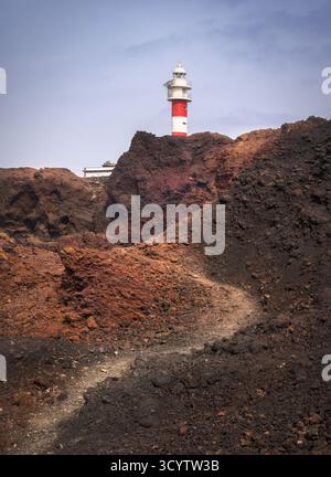 Ein markanter Leuchtturm steht vor der Kulisse von zerklüfteten Vulkanfelsen in der Nähe von Punta de Teno im sonnigen Teneriffa, Spanien Stockfoto