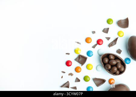Osterei mit gebrochener Schokolade und bunten Bonbons auf weißem Hintergrund. Ein verspieltes und festliches Setting für Ostern und Süßigkeiten. Stockfoto