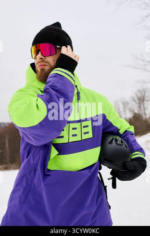 Ein Mann mit Bart genießt Snowboarden auf einer verschneiten Piste, während er bunte Oberbekleidung trägt. Stockfoto