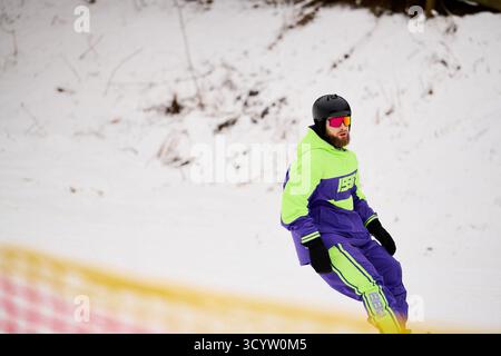 Ein bärtiger Mann genießt an einem Wintertag das Snowboarden auf einer verschneiten Piste, in hellem Gewand. Stockfoto
