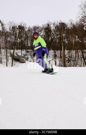 Snowboarder mit Bart genießen eine aufregende Fahrt auf einem verschneiten Hang umgeben von Bäumen. Stockfoto