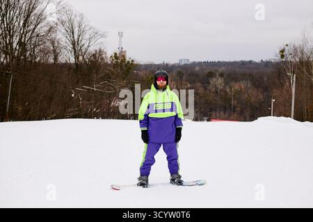Ein bärtiger Mann genießt Snowboarden auf einer verschneiten Piste, während er bunte Winterkleidung trägt. Stockfoto