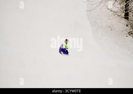 Ein bärtiger Mann genießt an einem klaren Wintertag Snowboarden auf einer verschneiten Piste. Stockfoto