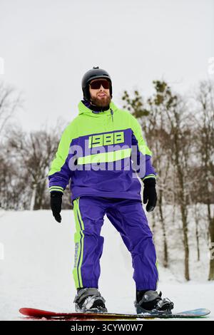 Ein bärtiger Mann genießt das Snowboarden auf einem verschneiten Pisten, umgeben von Winterbäumen und kühlem Wetter. Stockfoto