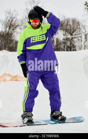 Ein bärtiger Mann in markanter Oberbekleidung genießt die Winterkälte beim Snowboarden auf einer Piste. Stockfoto