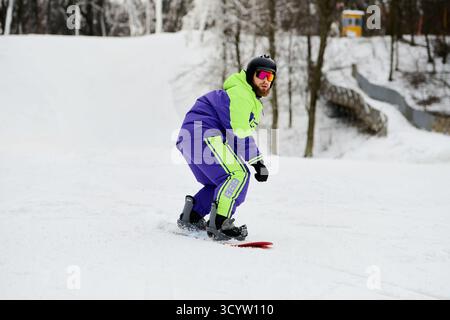 Ein bärtiger Mann genießt Snowboarden auf einer verschneiten Piste und zeigt sein Können im Wintersport. Stockfoto