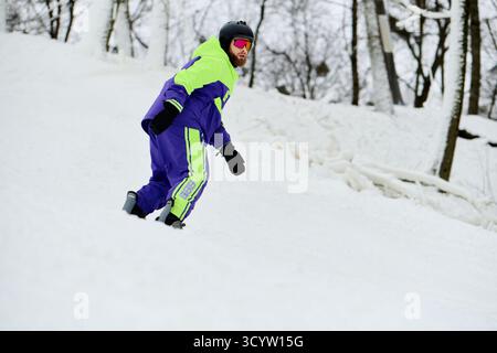 Ein bärtiger Mann genießt Snowboarden auf einer verschneiten Piste und zeigt sein Können und seine Winterkleidung. Stockfoto