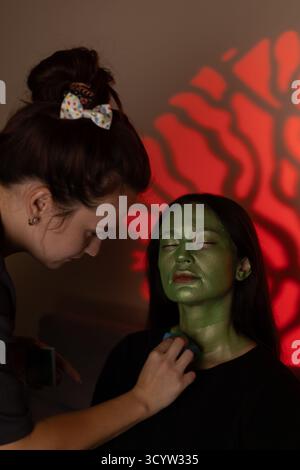 Ein Make-up-Künstler trägt grüne Gesichtsfarbe auf ein Model auf, um ein Halloween zu kreieren Stockfoto