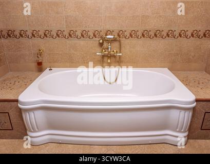 Opulente und einladende Badewanne in einem wunderschön gefliesten Badezimmer mit Vintage-inspirierten Goldarmaturen und einer geräumigen Badewanne, die perfekt für einen geeignet ist Stockfoto