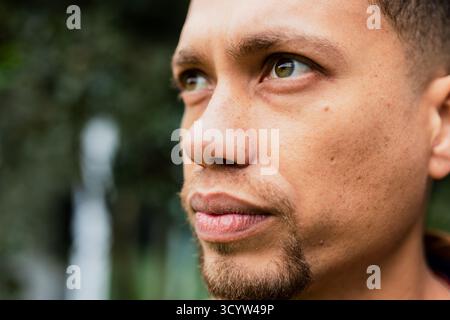 Mann, der im grünen Park zur Seite blickt, trägt bei Tageslicht einen dunklen Hoodie Stockfoto