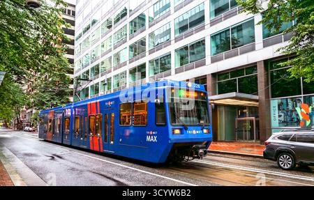 Portland, Oregon – 21. Juni 2025: An einem nassen, bewölkten Tag fährt ein TriMet MAX Stadtzug entlang einer von Bäumen gesäumten Straße im Zentrum der Stadt Stockfoto