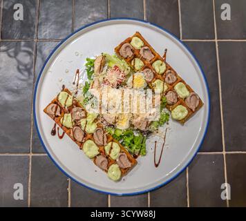 Gourmet-Caesar-Salat mit knusprigen belgischen Waffeln, Huhn, Eiern, Gurke und Balsamico-Nieseln auf weißem Teller Stockfoto
