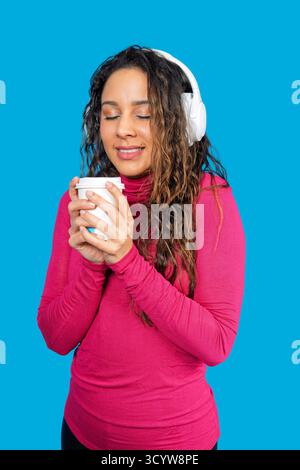 Frau schließt die Augen und lächelt, während sie Musik hört und eine warme Tasse hält Stockfoto
