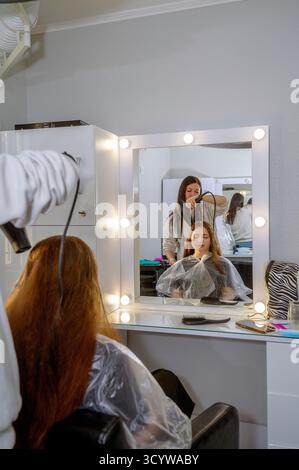 Die Kosmetikerin föhnt die Haare der Frau nach einem neuen Haarschnitt im Salon Stockfoto