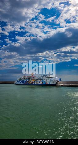 Eine Moby Lines Fähre im toskanischen Hafen. Im Hintergrund - blauer Himmel und weiße Wolken, im Vordergrund leuchtendes smaragdgrünes Meer. September 2024 Stockfoto
