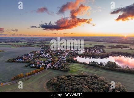 Das friedliche Dorf auf dem Land liegt eingebettet zwischen Feldern und Wäldern, mit einem reflektierenden See in der Nähe, der alle in das weiche, verblassende Licht eines bunten Su getaucht ist Stockfoto