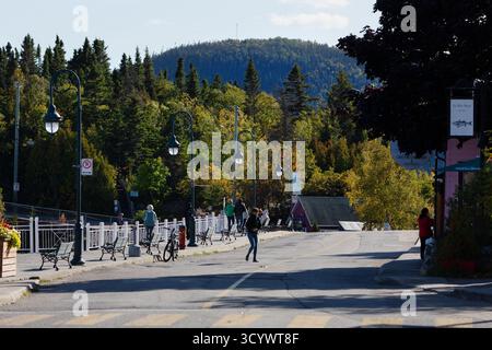 Die Menschen schlendern entlang der Hauptstraße in Tadoussac, Québec, umgeben von bewaldeten Hügeln und farbenfrohen Herbstlaub. Stockfoto