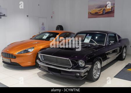 Metz, Frankreich - Blick auf einen violetten 1968 Ford Mustang GT Fastback in einem Showroom mit einem orangefarbenen Aston Martin Virage. Stockfoto