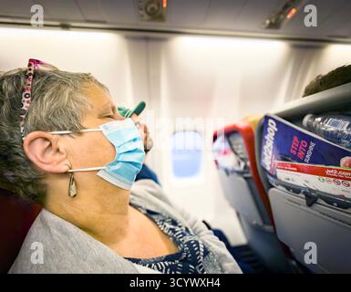 Weibliche Passagierin mittleren Alters mit Maske, die bei Tageslicht in einem Jet2-Flugzeug schläft und Sonnenlicht durch das Fenster kommt Stockfoto