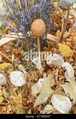 Eine rustikale Herbstkomposition mit getrocknetem Lavendel, Samenkapseln und einer Walnuss auf einem Stock zwischen Weizen und verblassten Blumen. Die Nahaufnahme zeigt komplizierte Details Stockfoto