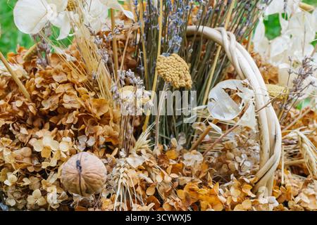 Eine detaillierte Komposition aus getrockneten Blumen und Kräutern in einem Korbkorb auf dem Gras. Das sanfte Sonnenlicht und die Erdtöne heben die rustikale Textur hervor Stockfoto