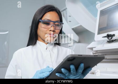 Porträt einer hübschen asiatischen Frau, einem Laborwissenschaftler, der ein Tablet hält, während er auf das Ergebnis des Biochemie-Analysators wartet. Stockfoto
