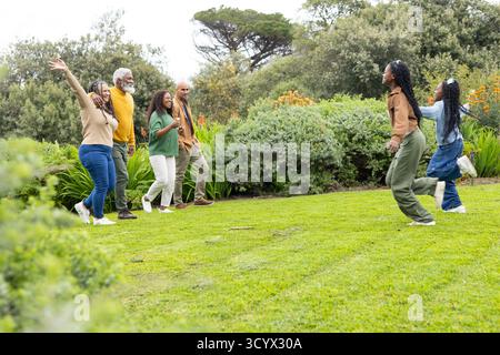 Vielfältige, generationenübergreifende Familienspaziergänge und -winken auf dem Rasen im Garten mit Einwegbecher Stockfoto