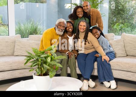 Afroamerikanische Familie trifft sich auf beigefarbenem Sofa im Wohnzimmer mit großen Fenstern Stockfoto