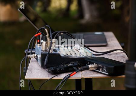 Eine professionelle Audioaufzeichnung mit schwarzem Audiomischer, Digitalrecorder und Mikrofonen, die auf einem rustikalen Holztisch inmitten eines vib positioniert sind Stockfoto