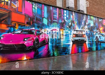 Farbenfrohes Stadtgemälde mit Sportwagen und einer neonfarbenen Stadtszene mit Fußgängern, die Regenschirme in der Regentnacht in Belfast Nordirland halten Stockfoto