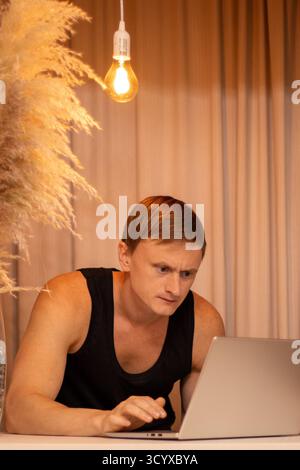 Nachdenklicher junger Mann im Spannungsfeld Analyse von Marktdiagrammen und Handelsdaten für Kryptowährungen auf Laptop im modernen Home Office Workspace. Unternehmen, Mann. Stockfoto