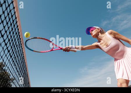 Tiefwinkelaktion einer Tennissportlerin, die mit Schläger und Ball ins Netz geht, gegen Training und Fokus des blauen Himmels Stockfoto