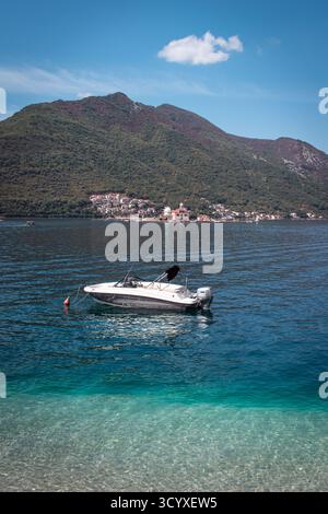 Eine atemberaubende Küstenlandschaft mit einem kleinen Motorboot, das auf der ruhigen Adria in der Nähe des Ufers schwimmt. Ein malerisches Dorf schmiegt sich an Berge. Stockfoto