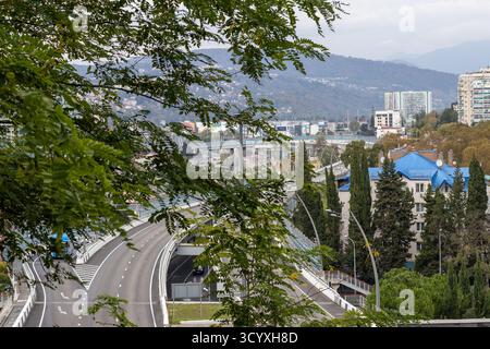 Highway, der sich durch die Stadtlandschaft schlängelt. Aus der Vogelperspektive einer mehrspurigen Autobahn, die sich durch ein Stadtgebiet mit Bäumen, Gebäuden mit blauem Dach und weit entfernten Gebäuden führt Stockfoto