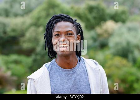 Afroamerikanischer Mann, der im Park steht und grauen Zip-Up Hoodie Heather Blue T-Shirt Creolen trägt Stockfoto