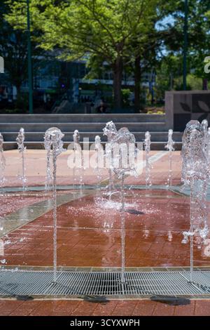 Aus nächster Nähe sehen Sie Wasserstrahlen vom Springbrunnen der Olympischen Ringe im Centennial Olympic Park, die unter hellem Sonnenlicht vor einem Hintergrund von Bäumen glitzern Stockfoto