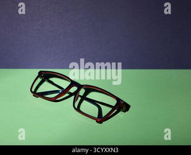 Eine Brille, die auf einer blauen und grünen Oberfläche mit heller Tageslicht-Simulation fotografiert wurde. Das klare Layout und die starken Schatten schaffen einen Beruf Stockfoto