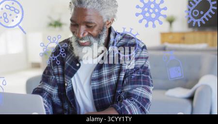Lächelnder Senior Afroamerikaner mit Fokus auf Laptop zu Hause, mit Virus-Icons und Desinfektionsmittel Stockfoto