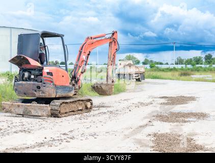Ein orangefarbener Minibagger (Bagger) mit einem einzigen Fahrer steht auf einer Schotterstraße, nachdem er vor kurzem kleine Schmutzhaufen ausgehoben und bewegt hat. Stockfoto