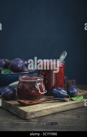 Pflaumenmarmelade in Glasgläsern mit Reifen Pflaumen auf dunklem Hintergrund Stockfoto