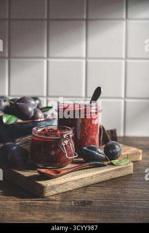 Pflaumenmarmelade in Glasgläsern mit Reifen Pflaumen auf hellem Hintergrund Stockfoto