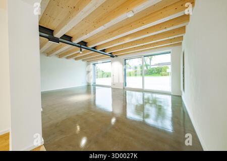 Großes, helles Wohnzimmer mit freiliegenden Holzbalken, poliertem Betonboden und großen Schiebetüren zum Garten, Hausrenovierung, Klimaanlage Stockfoto
