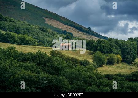 Einsames traditionelles Steinbauhaus auf Rolling Green Hills mit Wald, dramatischen Sturmwolken und ländlicher Berglandschaft Stockfoto