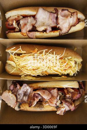 Amerikanischer Hotdog mit verschiedenen Geschmacksrichtungen, mit Käse und knusprigen Zwiebeln auf einem weißen Tisch in minimalistischem Stil. Fast Food, Essen zum Mitnehmen, Essen für Moto Stockfoto