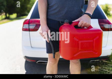Ein Mann hält einen roten Kanister in der Nähe eines weißen Wagens, Nahaufnahme. Stopp zum Tanken, kein Tanken, Kraftstoffprobleme Stockfoto