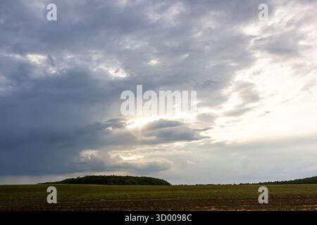 Dunkle Wolken sammeln sich über einem weiten, offenen Feld, wenn das Tageslicht nachlässt, und schaffen eine stimmungsvolle und fesselnde Atmosphäre, die ideal ist, um nat zu reflektieren und zu schätzen Stockfoto